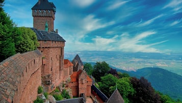 Een historisch kasteel met een opvallende toren, omgeven door weelderige begroeiing en met een panoramisch uitzicht op het landschap.