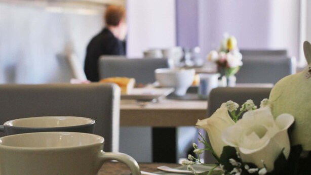 A dining area with tables set for meals, including plates, cups, and a vase with flowers. - Hôtel Le Dormeur (Dorlisheim)