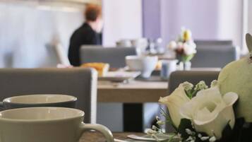 Comedor con mesas dispuestas para comidas, incluyendo platos, tazas y un jarrón con flores.