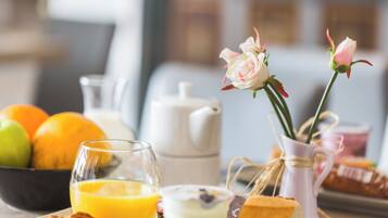 Desayuno con cruasanes, jugo de naranja, un vaso de leche, una tetera y un florero con flores.