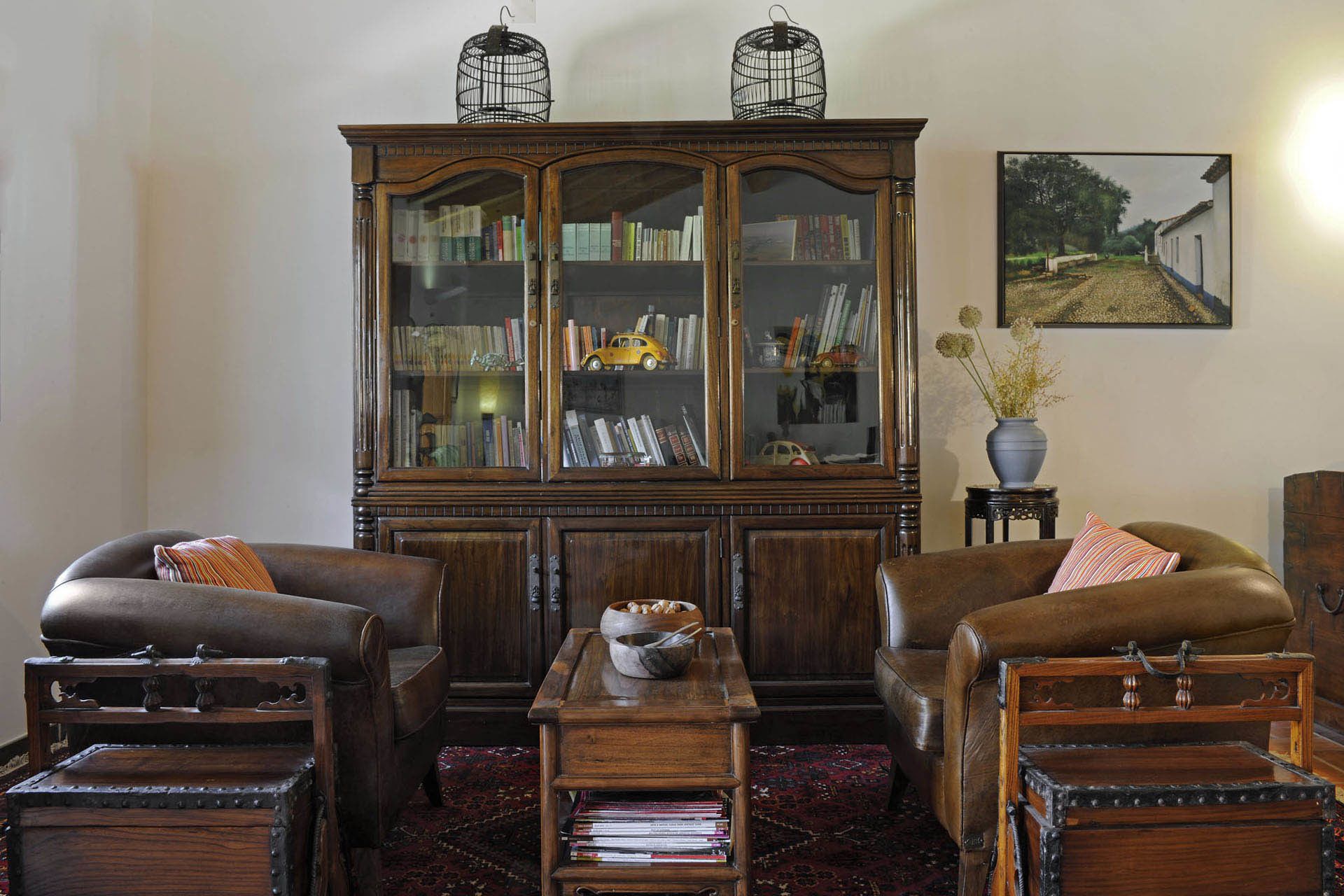 Ein traditionell eingerichtetes Wohnzimmer mit Ledersesseln, einem Holztisch, einem Bücherregal und einem alten Koffer.