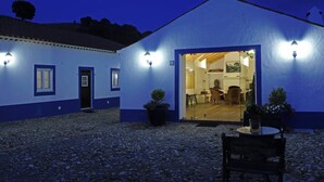 A building with a white exterior and blue trim, featuring a door leading to an interior space with a dining area and a visible kitchen. - Quinta do Chocalhinho (Odemira)