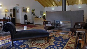 A spacious lobby with a high ceiling, a fireplace, and a variety of seating options including a plush armchair and a bar stool. - Quinta do Chocalhinho (Odemira)