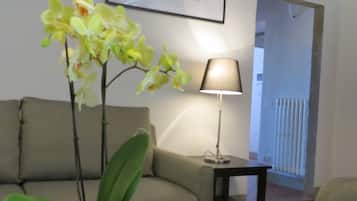 A living room with a sofa, a coffee table with a book, a lamp, and an orchid plant.