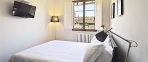 A bedroom with a bed, a TV mounted on the wall, a window with a view of buildings, and a radiator. - Toscanelli Residenza D'epoca (Florence)