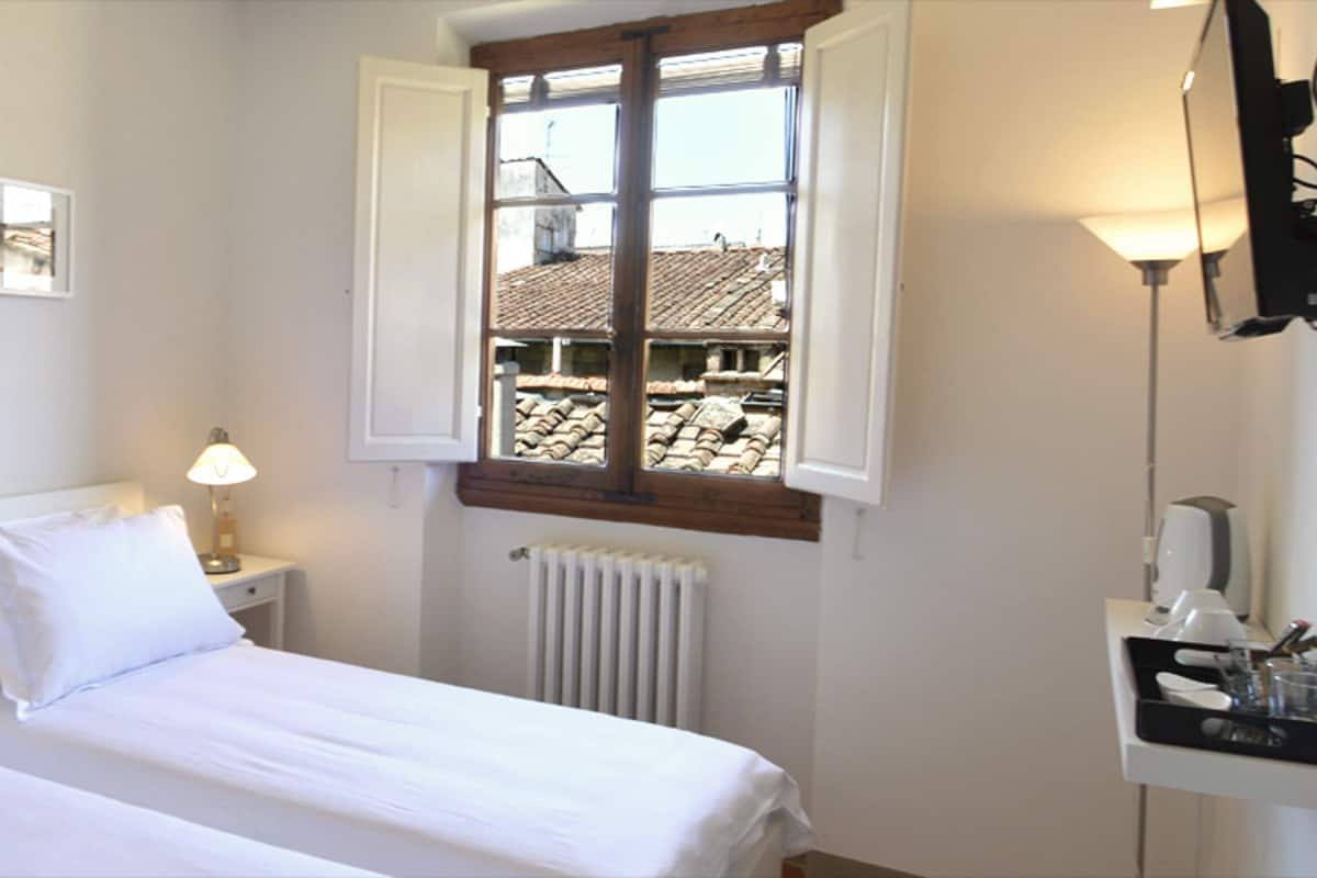 A bedroom with a bed, a nightstand, a lamp, a window, and a radiator.