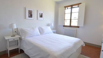 Ein helles Schlafzimmer mit einem Bett, zwei Nachttischen, einem Fenster und zwei gerahmten Bildern an der Wand.