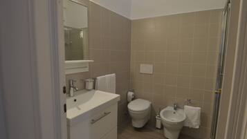 A bathroom with a sink, toilet, bidet, and mirror.
