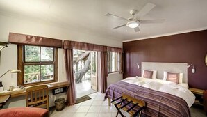 A bedroom with a bed, a desk, a chair, a ceiling fan, and a window with curtains.