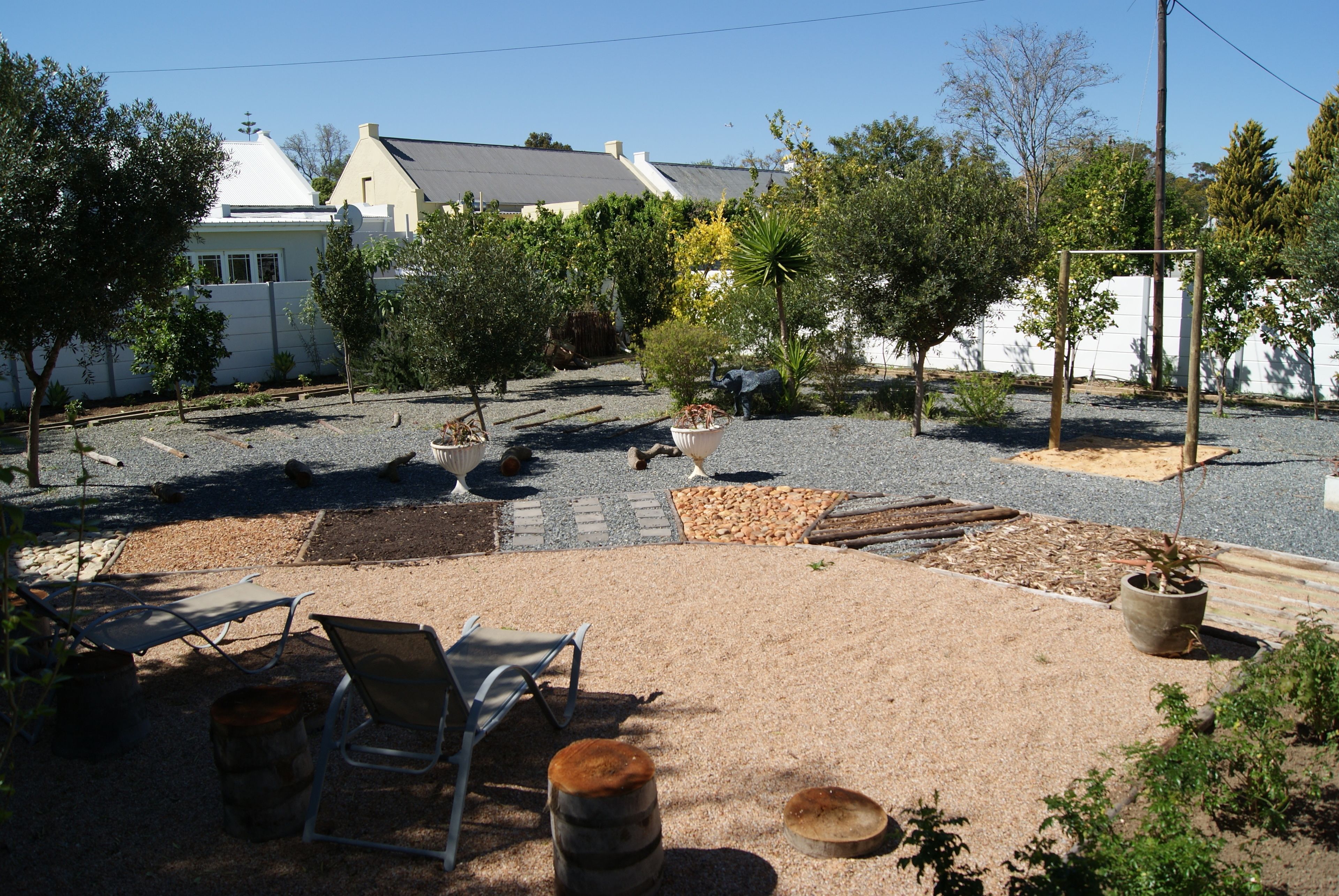 An outdoor patio area with a seating arrangement, a small garden, and a white building in the background.