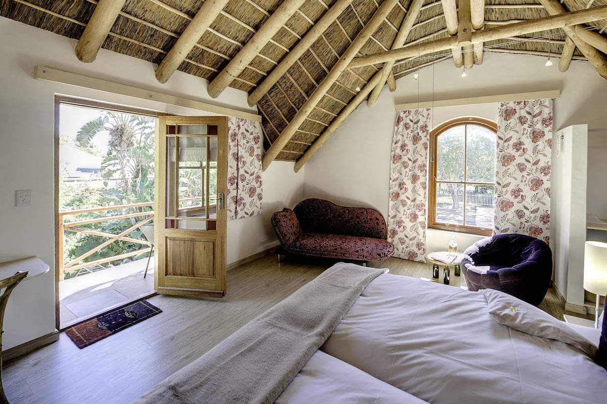 A bedroom with a sloped ceiling, a sofa, a bed, and a window with floral curtains.