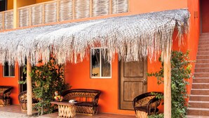 A two-story building with a thatched roof over a patio area, featuring wicker furniture and a wooden door. - B&B Casa Juarez (La Paz)