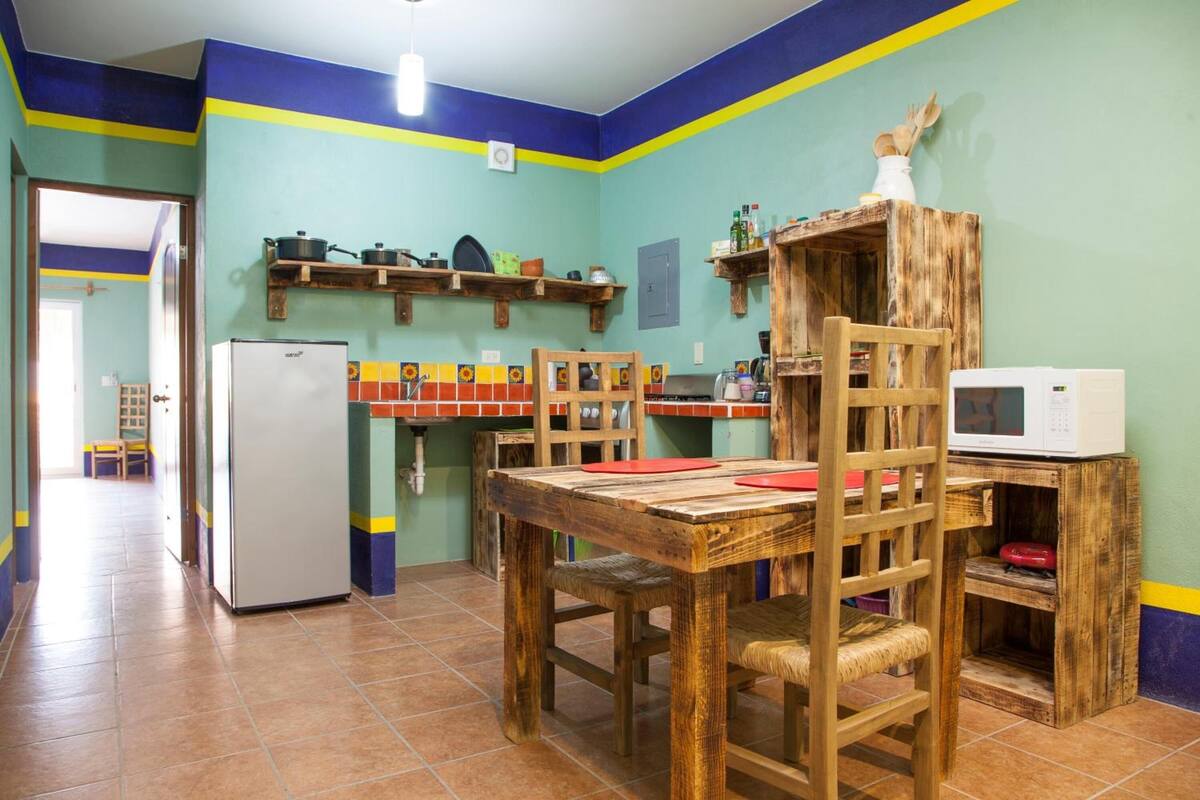 Una cocina con una mesa de madera, sillas, un refrigerador y un microondas.