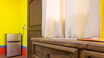 Una habitación con un armario de madera, un refrigerador pequeño y una cortina.