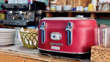 A vintage red toaster on a wooden table with a woven basket and stacked plates.
