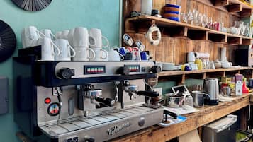 Een koffieapparaat op een houten aanrecht, met verschillende keukenbenodigdheden en een plank vol met glazen.