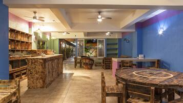 A spacious room with a large wooden dining table, a bar area with wooden shelves, and a ceiling fan.