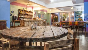 A rustic dining area with a wooden table and chairs, a bar with shelves of bottles and glasses, and a view of the outdoors through a glass door. - B&B Casa Juarez (La Paz)