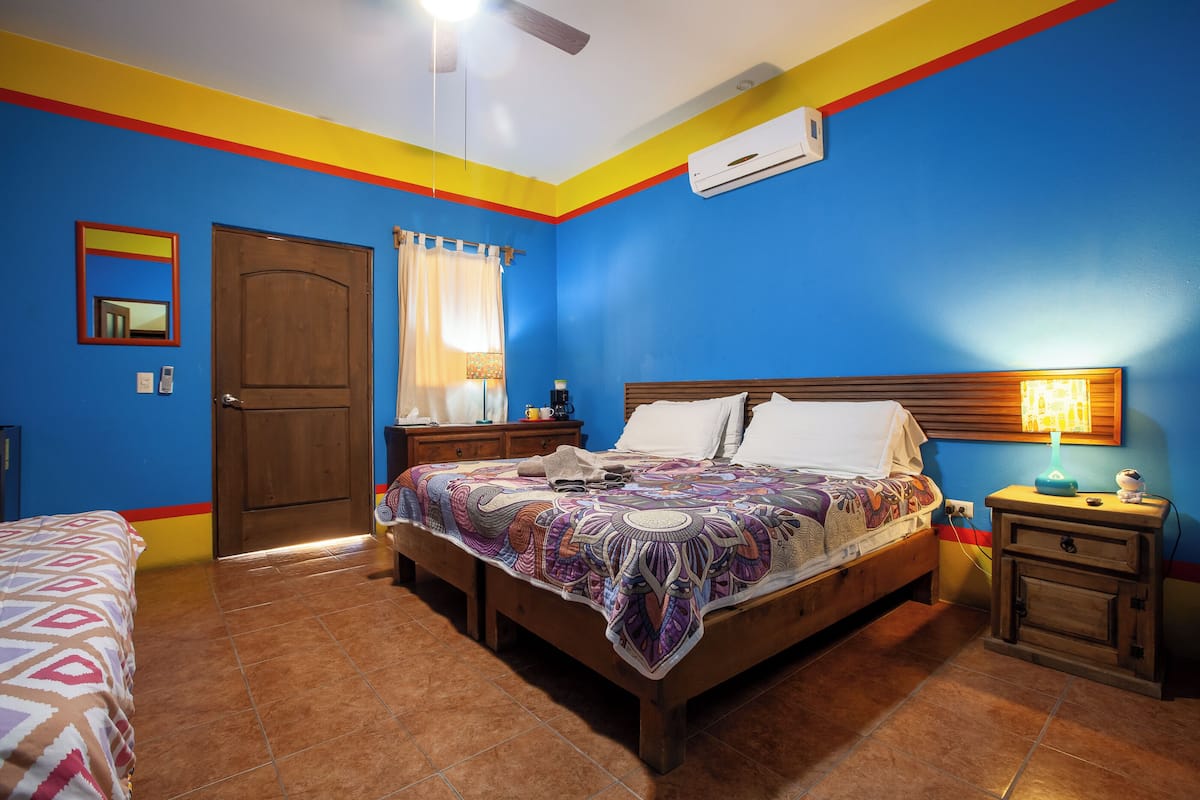 Un dormitorio con cama, mesitas de noche, espejo y aire acondicionado.