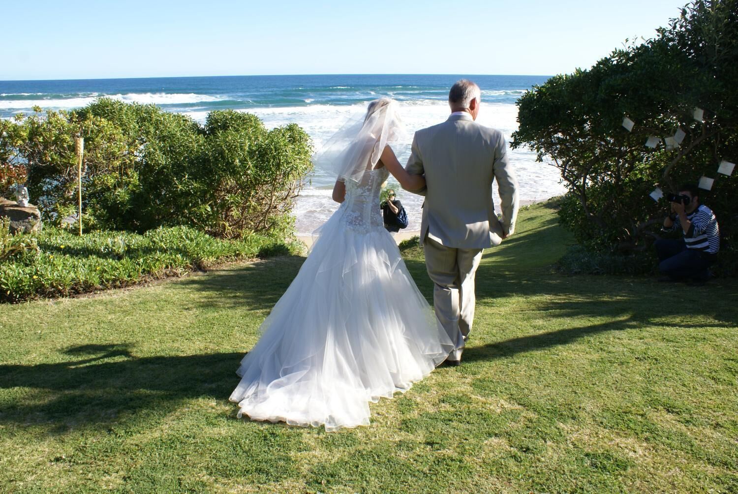 A couple walking on a grassy path with a view of the ocean.