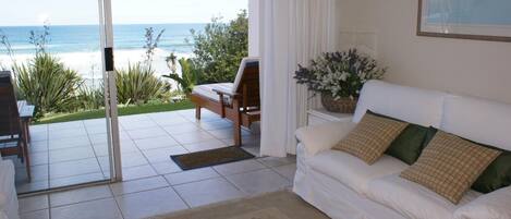 A living room with a white sofa, a wooden chair, and a view of the ocean through large glass doors.