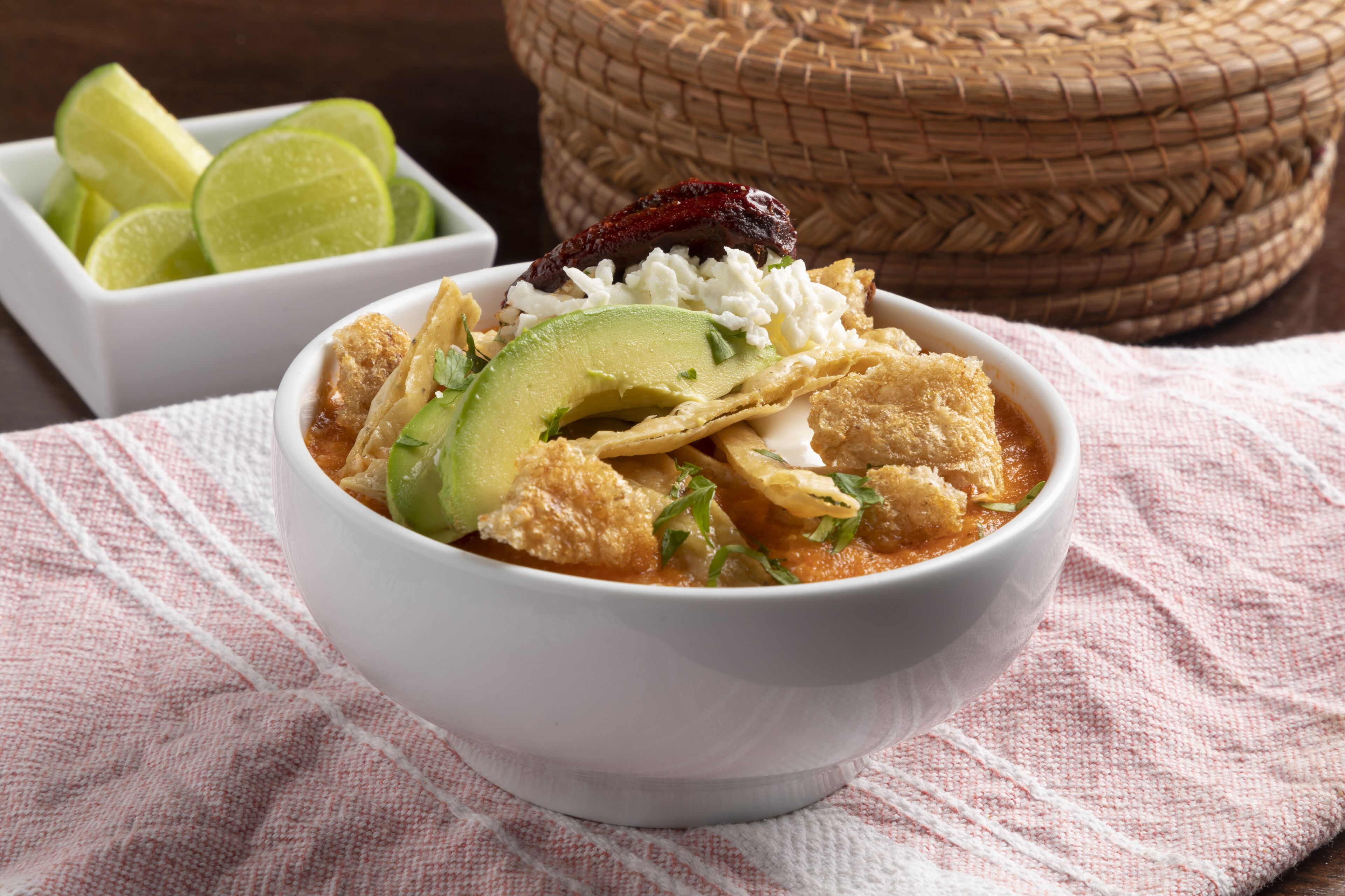 Un tazón de sopa con aguacate, totopos y un gajo de limón.