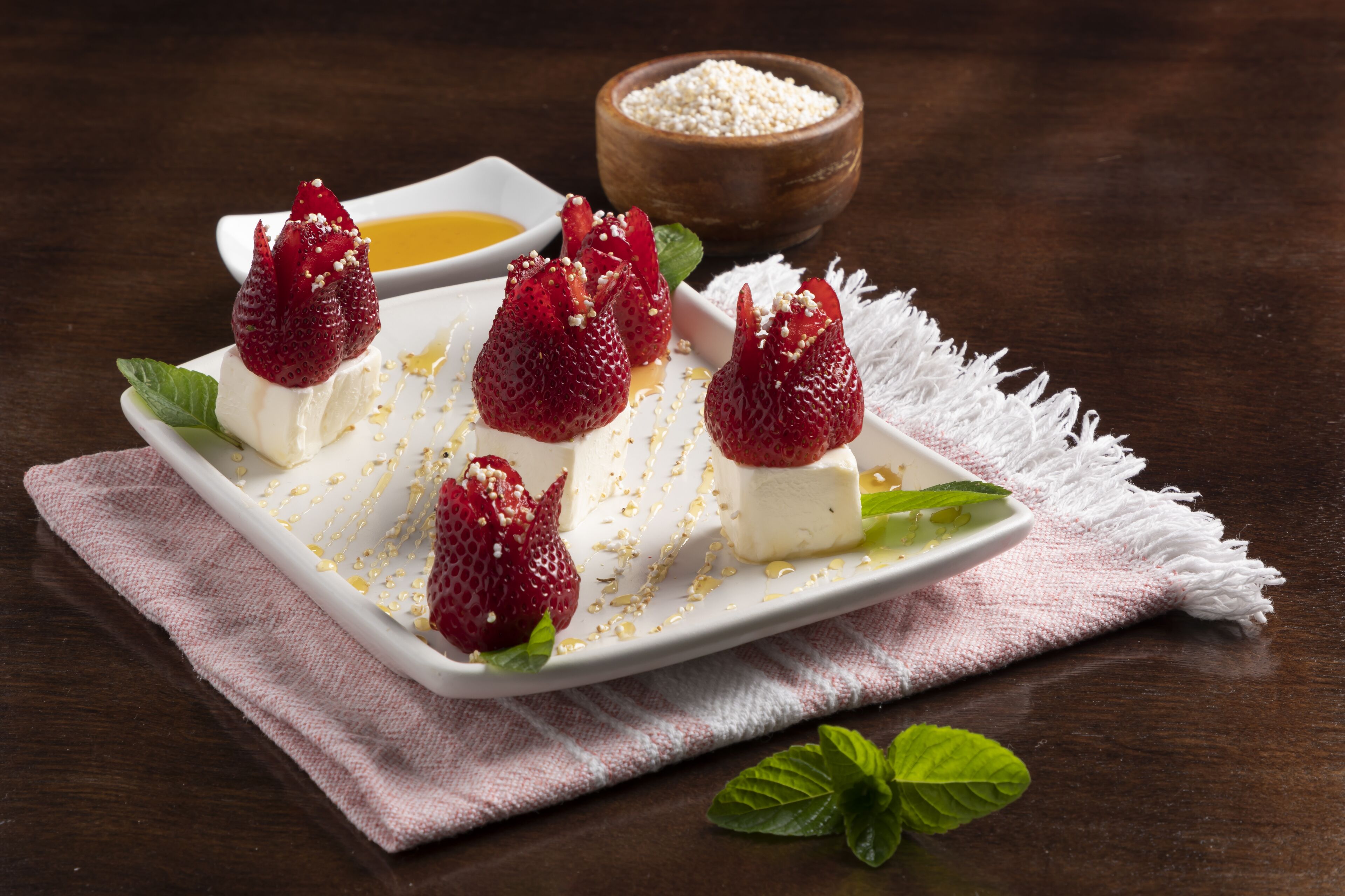 Un plato de postre con fresas y un recipiente pequeño de miel.