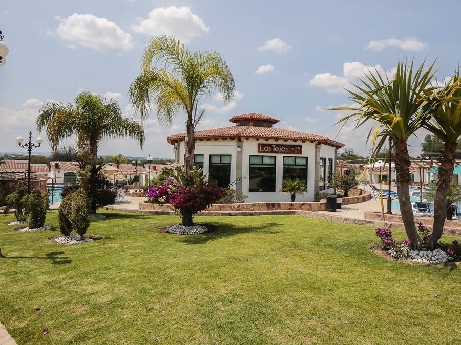 A building with a sign reading "Los Teques" surrounded by well-maintained lawns and palm trees.