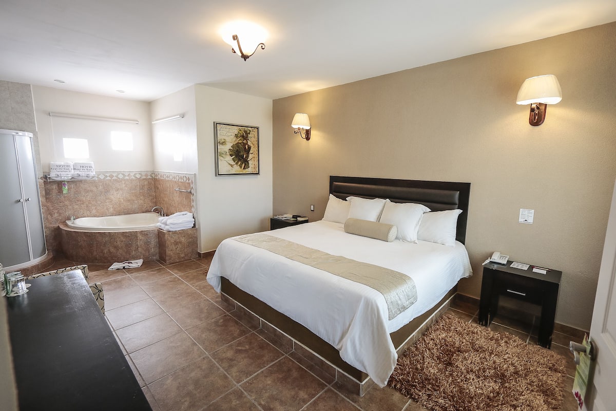 Ein Hotelzimmer mit einem großen Bett, einer Badewanne, einem Schminktisch mit Spiegel und zwei Wandlampen.
