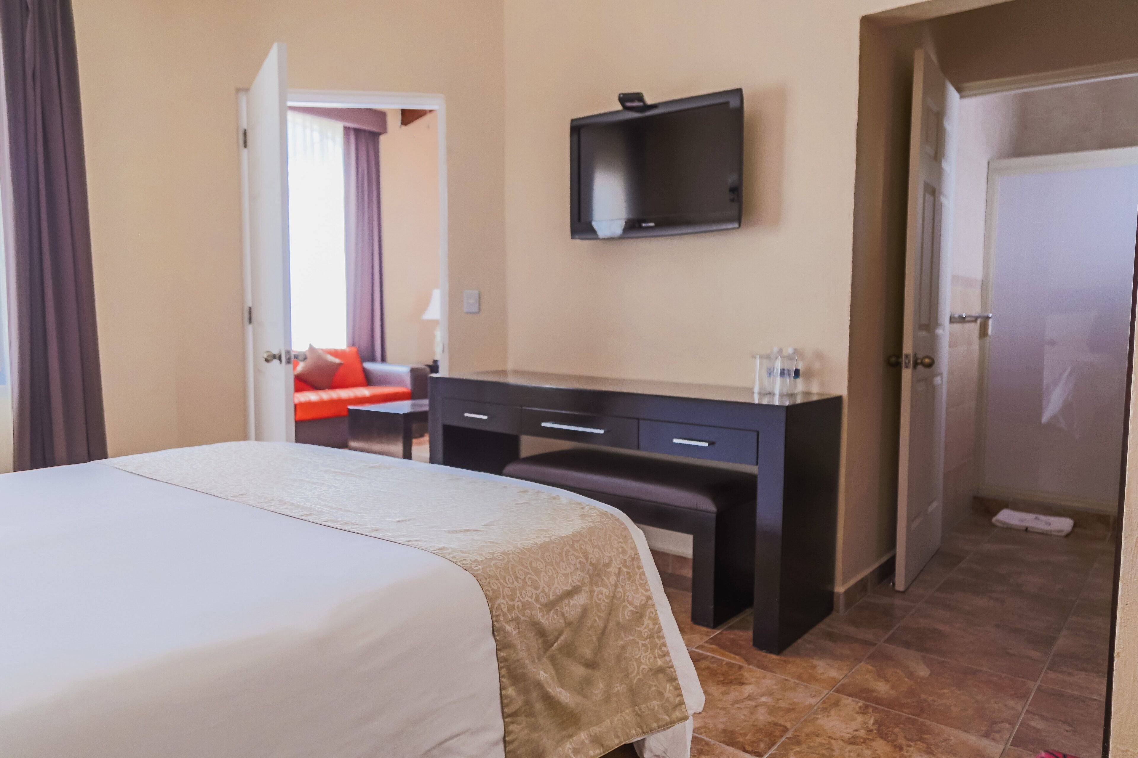 Una camera d'albergo con un letto, una scrivania, una sedia, una TV a parete e una porta che conduce a un'altra stanza.