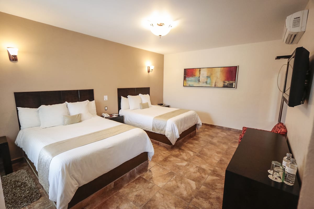 Ein Hotelzimmer mit zwei Betten, einem Schreibtisch, einem Fernseher und Bildern an der Wand.