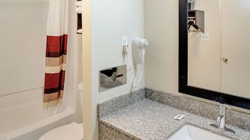 Un baño con inodoro, cortina de ducha, secador de pelo, lavamanos y espejo.