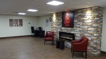 A reception area with a stone wall, a Red Roof Inn sign, a fireplace, and two leather chairs.