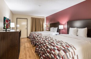 Habitación de hotel con dos camas, un televisor sobre un escritorio y la puerta del baño.