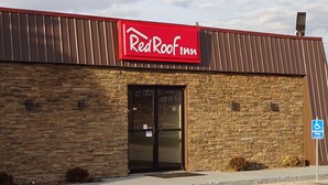 A RedRoof Inn building with a stone facade, a black entrance door, and a handicap parking sign.