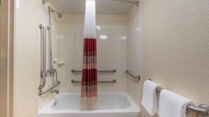 A bathroom with a white bathtub, a shower with a handheld showerhead, and a towel rack with a white towel.