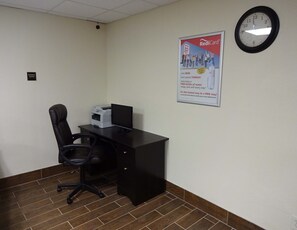 Un centro de negocios con escritorio, silla, impresora y un reloj en la pared.