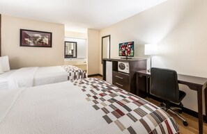 Ein Hotelzimmer mit zwei Betten, einem Schreibtisch mit Computer, einem Sessel und einem Fernseher.