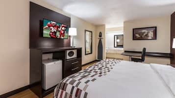 A hotel room with a bed, a television, a desk with a microwave, a chair, and a small refrigerator.