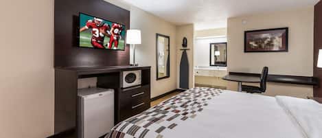 A hotel room with a bed, a television, a desk with a microwave, a chair, and a small refrigerator.
