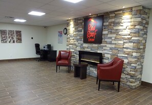 Un hall con pared de piedra, chimenea, sillones de cuero, mostrador de recepción y un reloj.