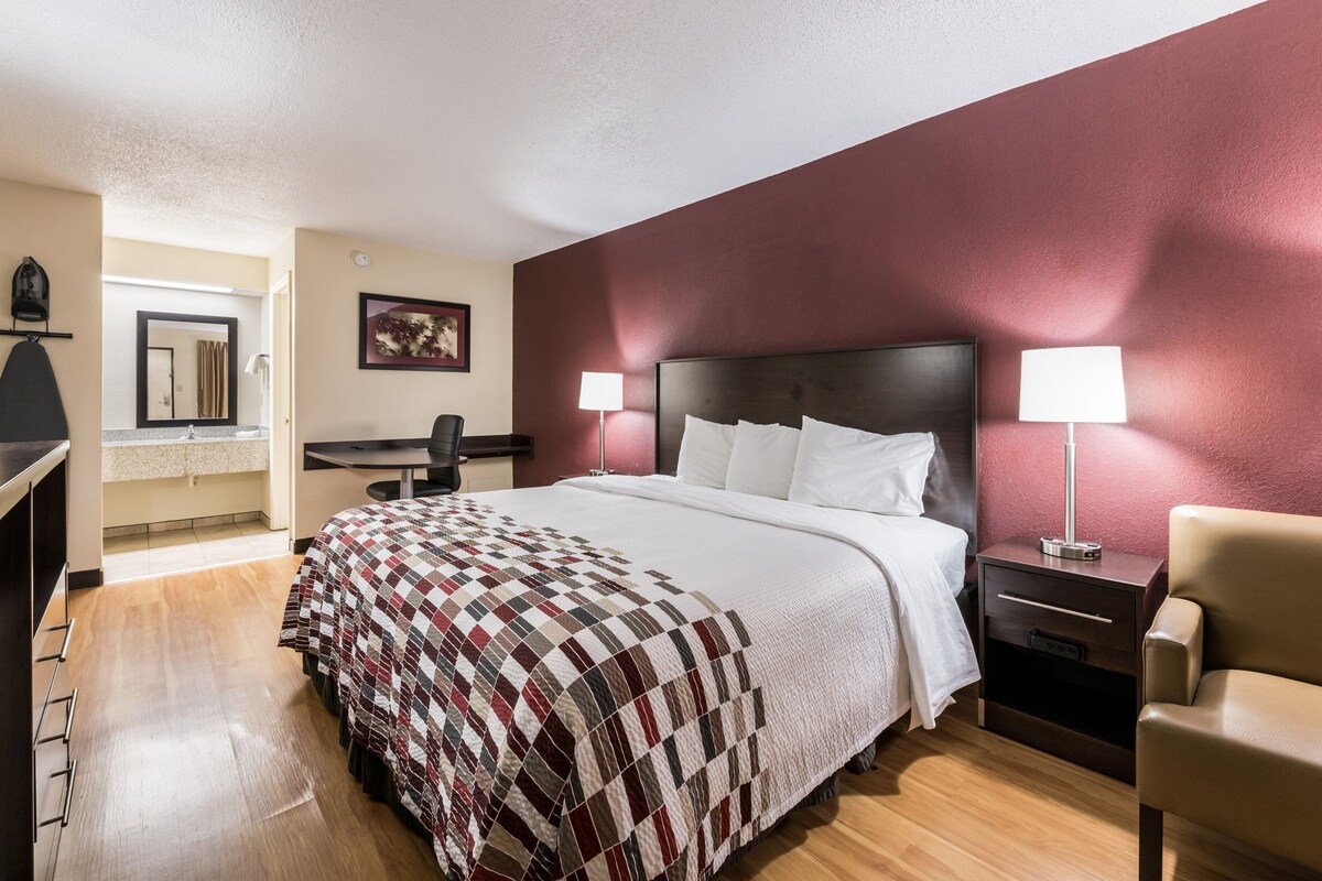 Una habitación de hotel con cama, mesitas de noche, escritorio, silla y espejo.