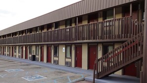 A motel with a two-story structure, multiple rooms with red doors, and a parking area with handicapped parking spaces.