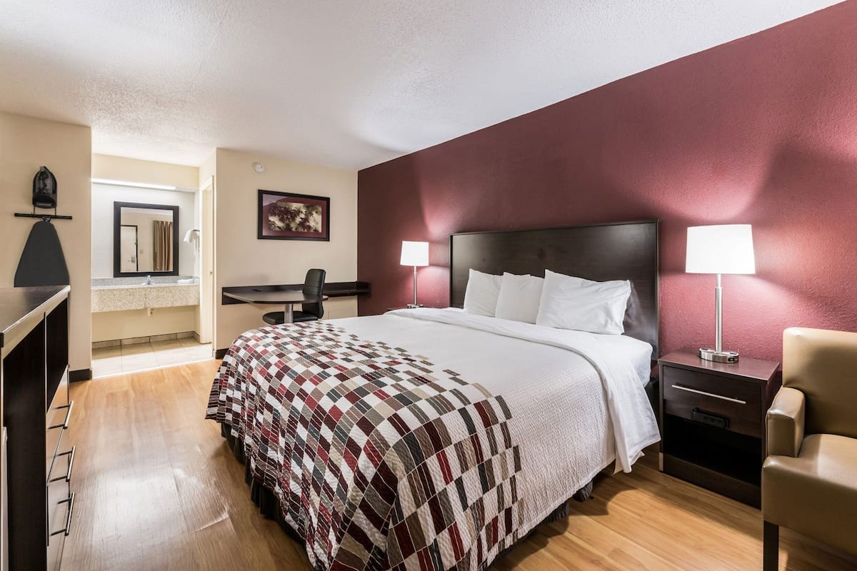 A hotel room with a bed, desk, chair, and nightstand.