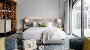 A modern hotel room with a large bed, bedside tables, a wardrobe, and a view through a large window.