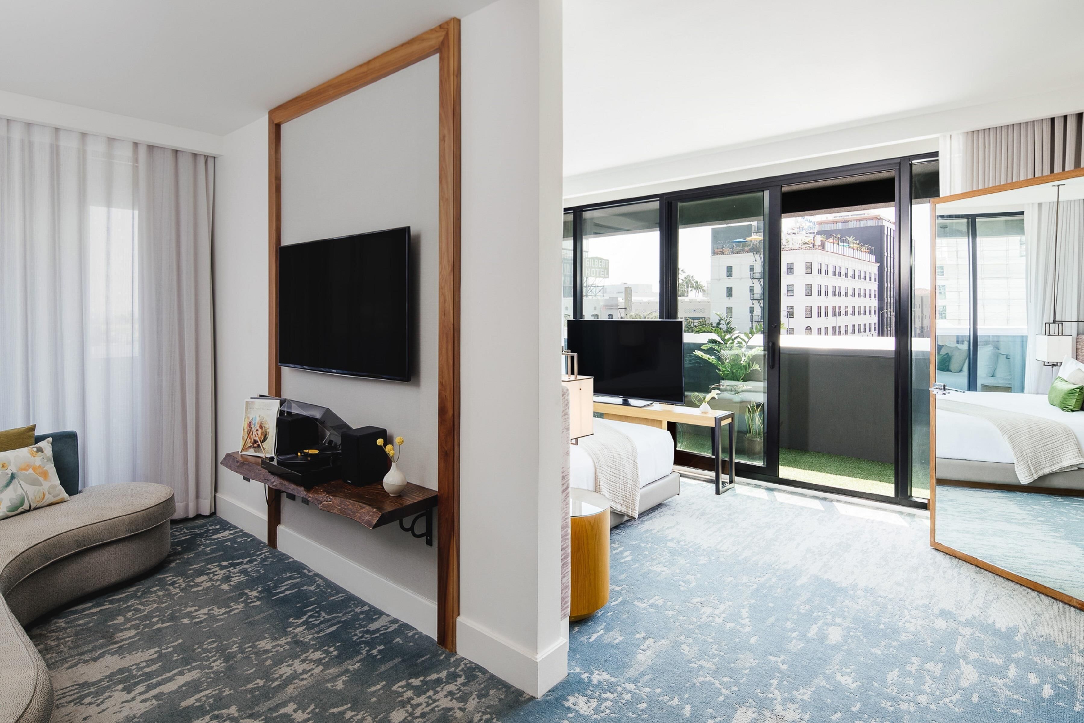 A hotel room with a sofa, a flat-screen TV, a bed, a desk, and a large window with a city view.
