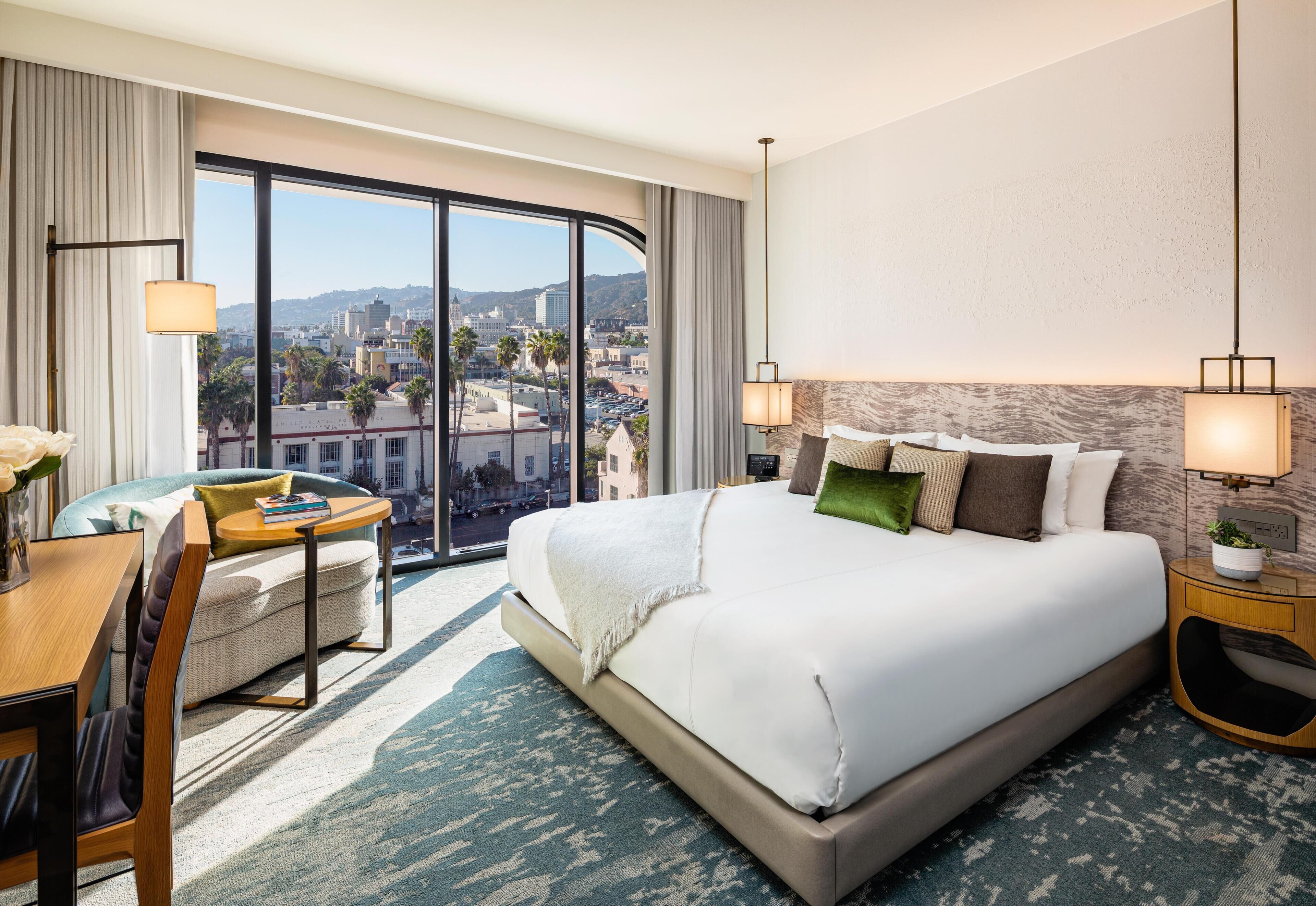 Une chambre d’hôtel avec un grand lit, un bureau, une chaise, une vue sur la ville et une grande fenêtre.