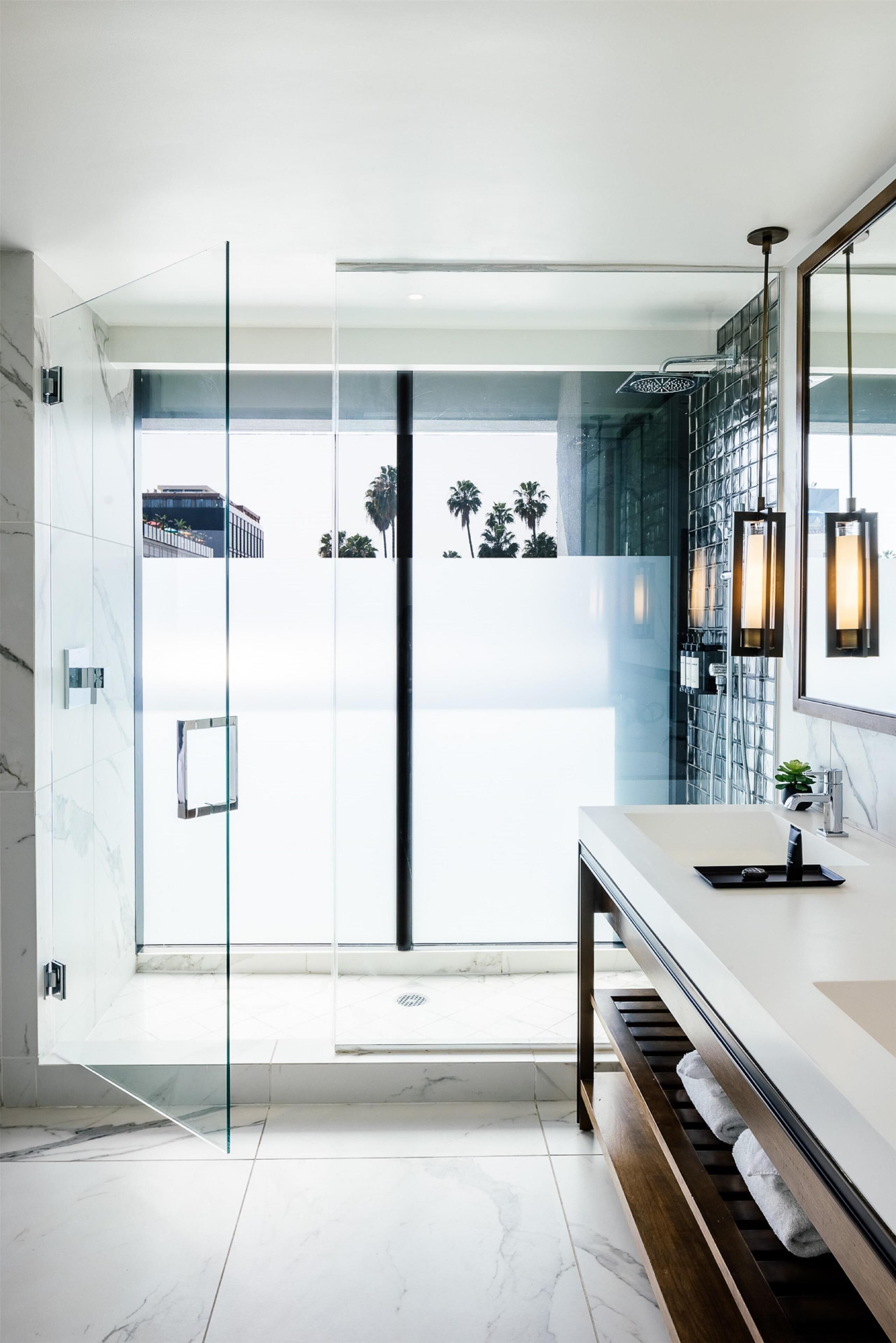A modern bathroom with a glass shower enclosure, a marble-tiled floor, a wooden vanity, and a large mirror.