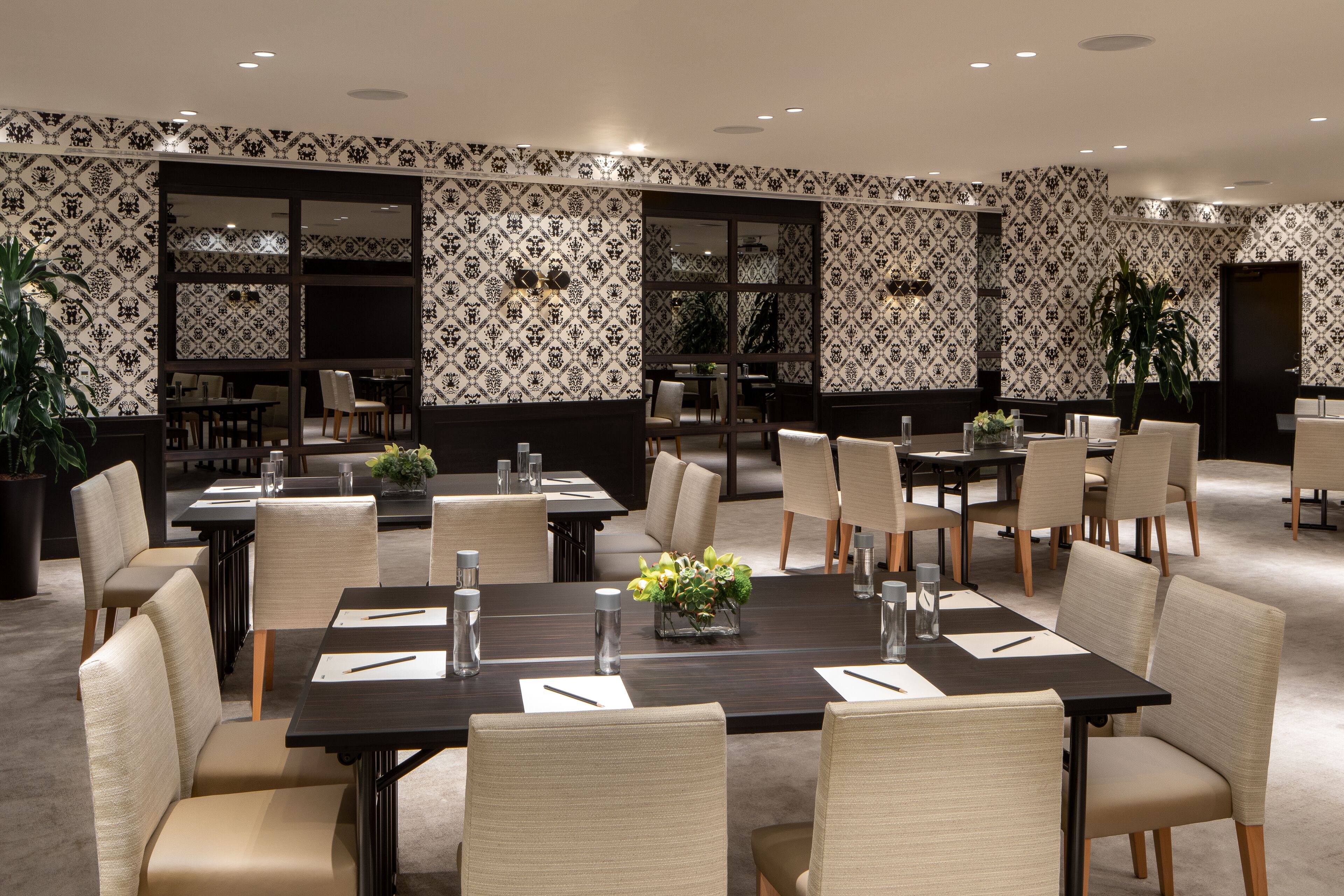 A conference room with multiple tables and chairs, patterned wallpaper, and large windows.
