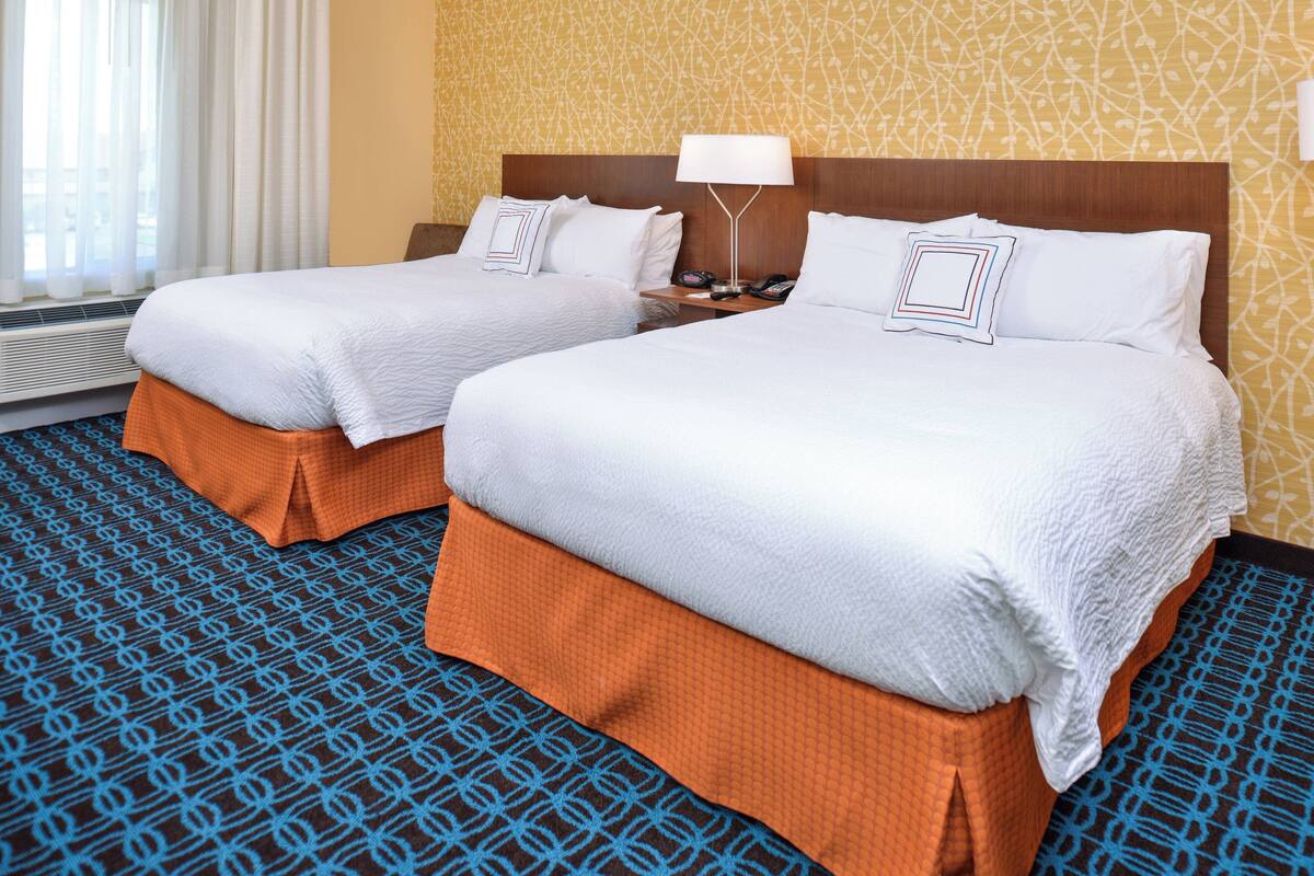 A hotel room with two beds, a nightstand with a lamp, and a patterned carpet.